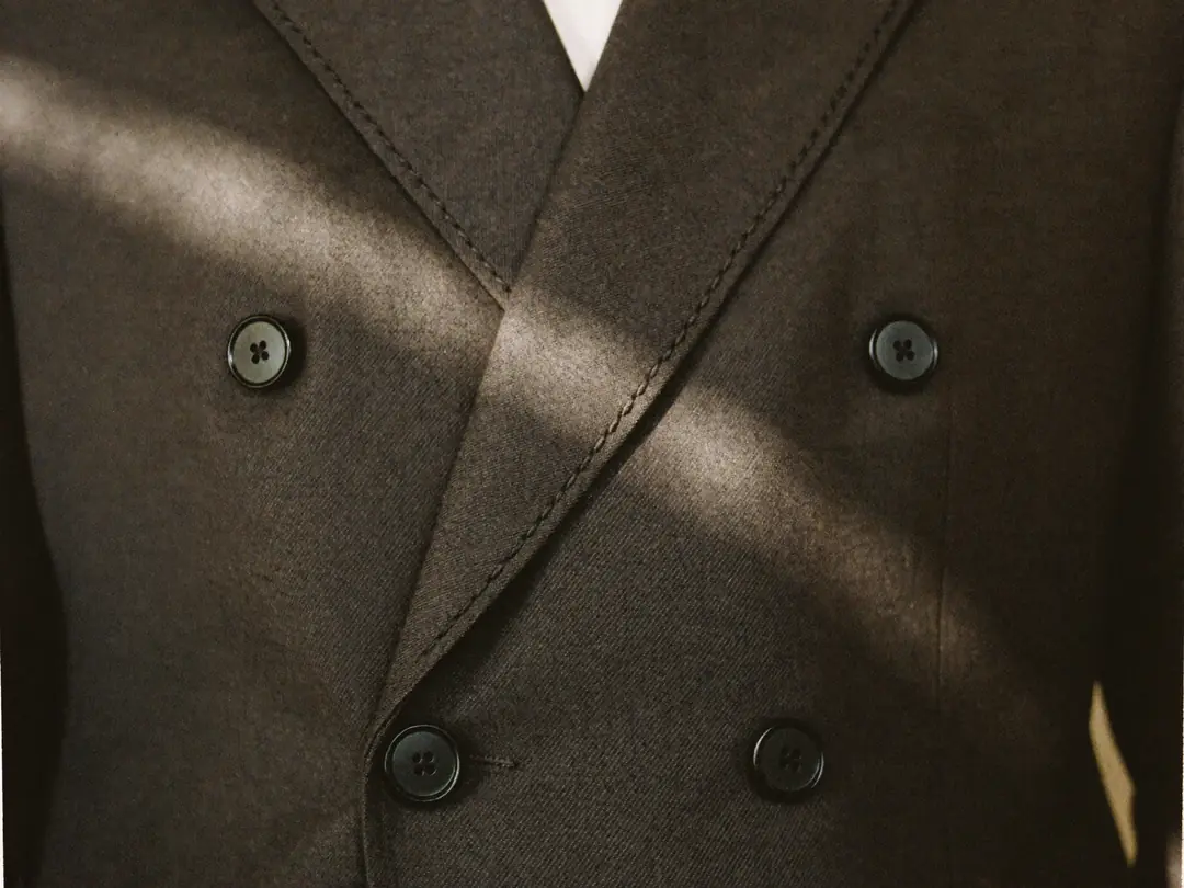 Window light across the lapel stitching and buttons of a double-breasted blazer